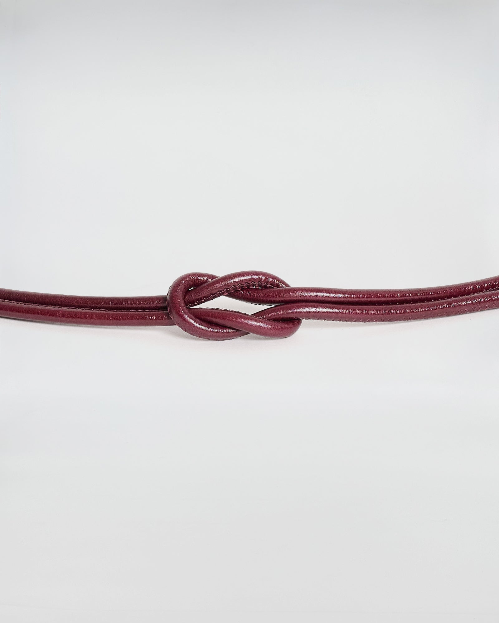 Cintura tubolare in pelle con terminale in metallo, design elegante e distintivo.