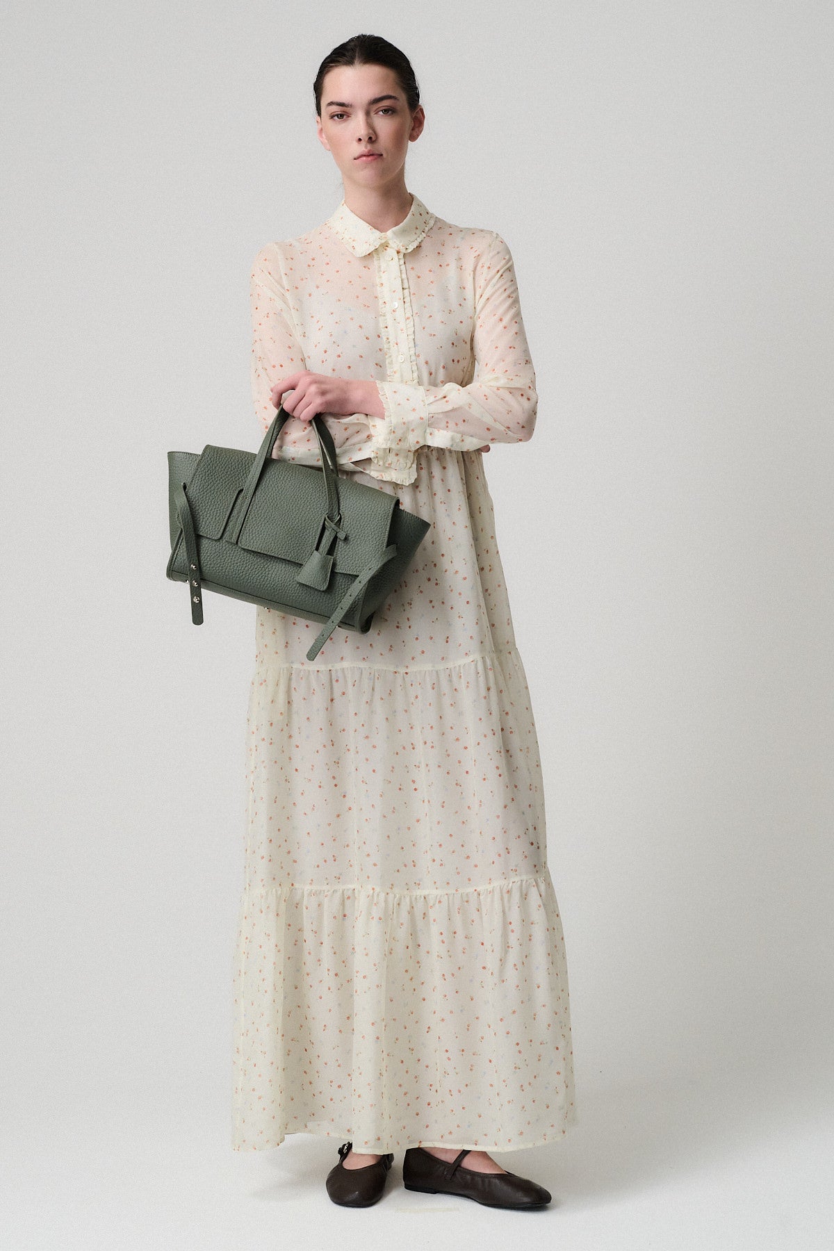 PENNY SMALL VITELLO in green held by a model wearing a floral maxi dress, showcasing elegance and versatility.