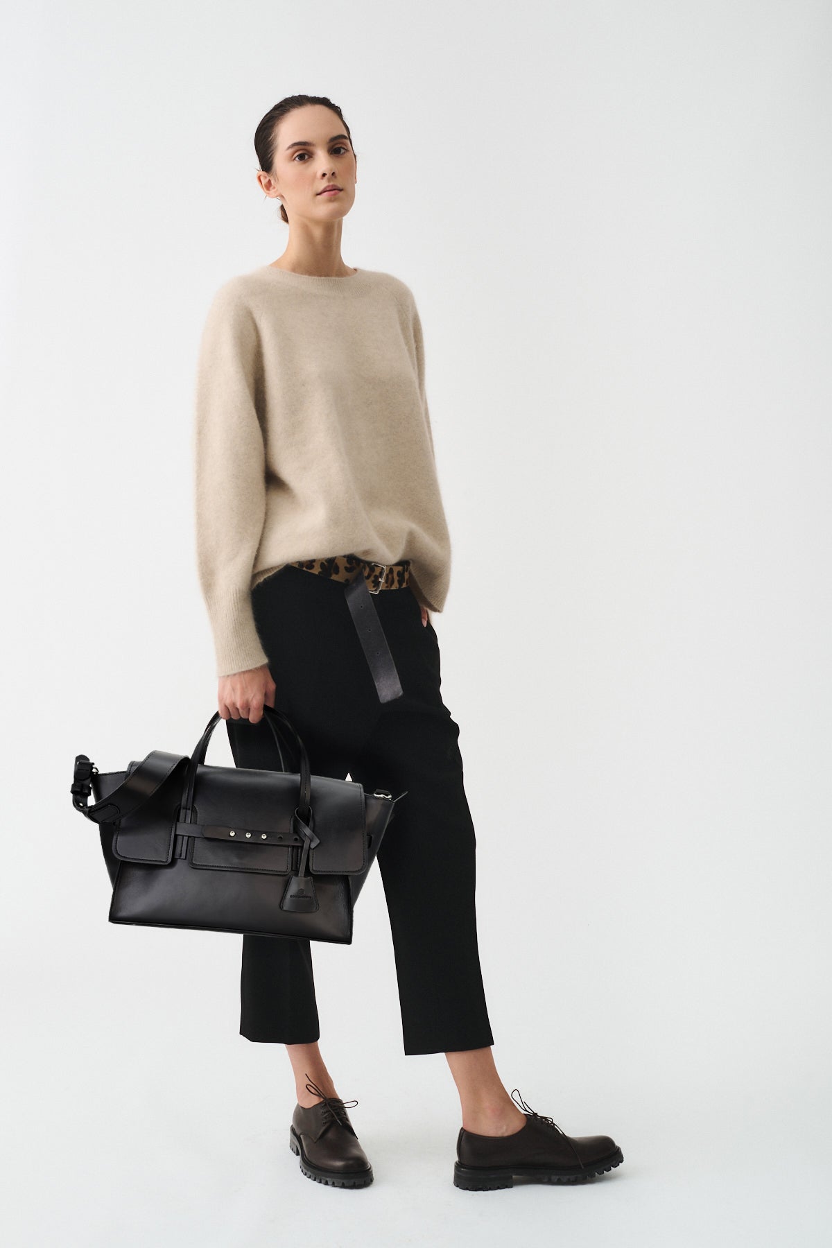 Model showcasing the stylish Penny Medium Vitello bag, paired with a beige sweater and black pants in a modern setting.