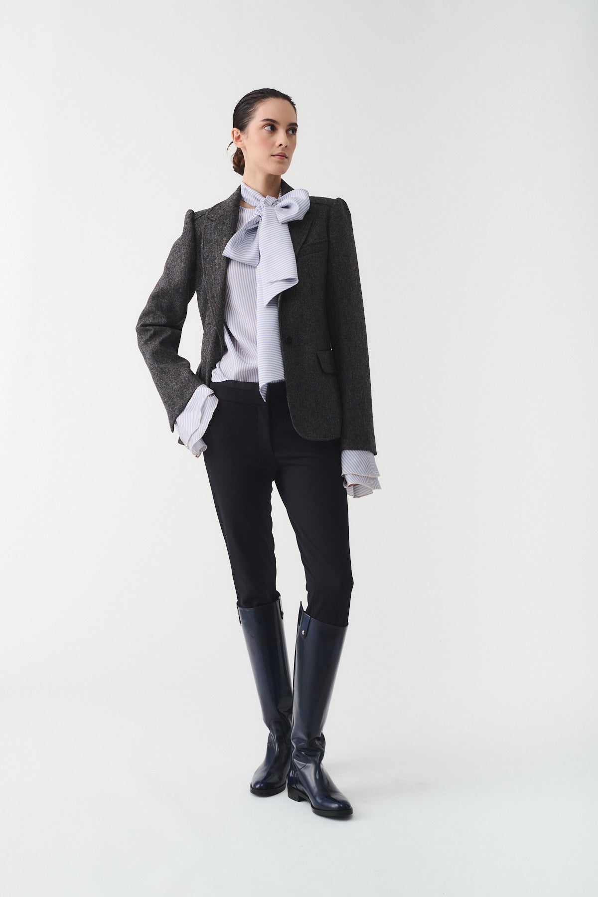 GIACCA MONOPETTO LORD indossata da una donna elegante, con giacca monopetto grigia e pantaloni neri, in piedi su sfondo chiaro.
