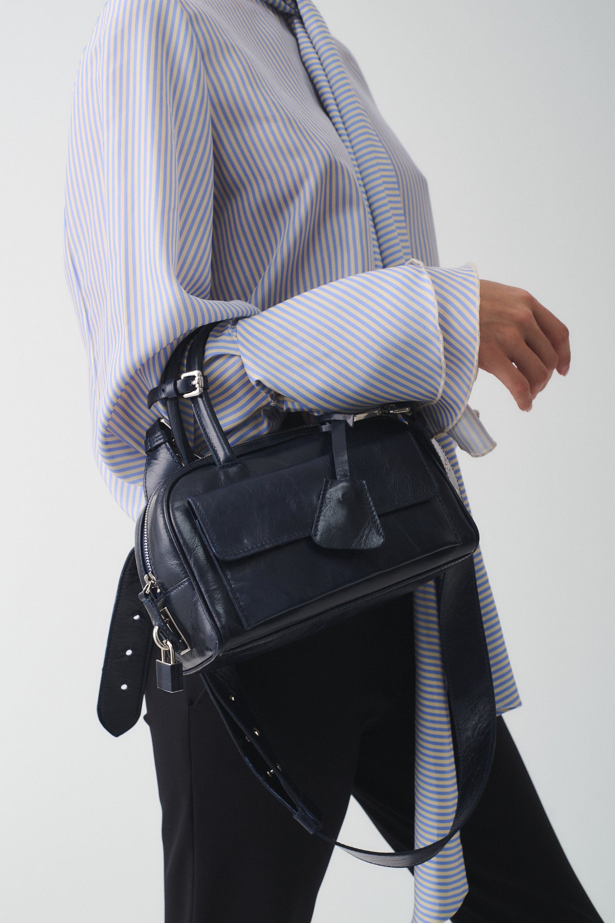 Zoe Mini Vitello Semilucido handbag held by a woman in a stylish striped shirt, showcasing its elegant design.