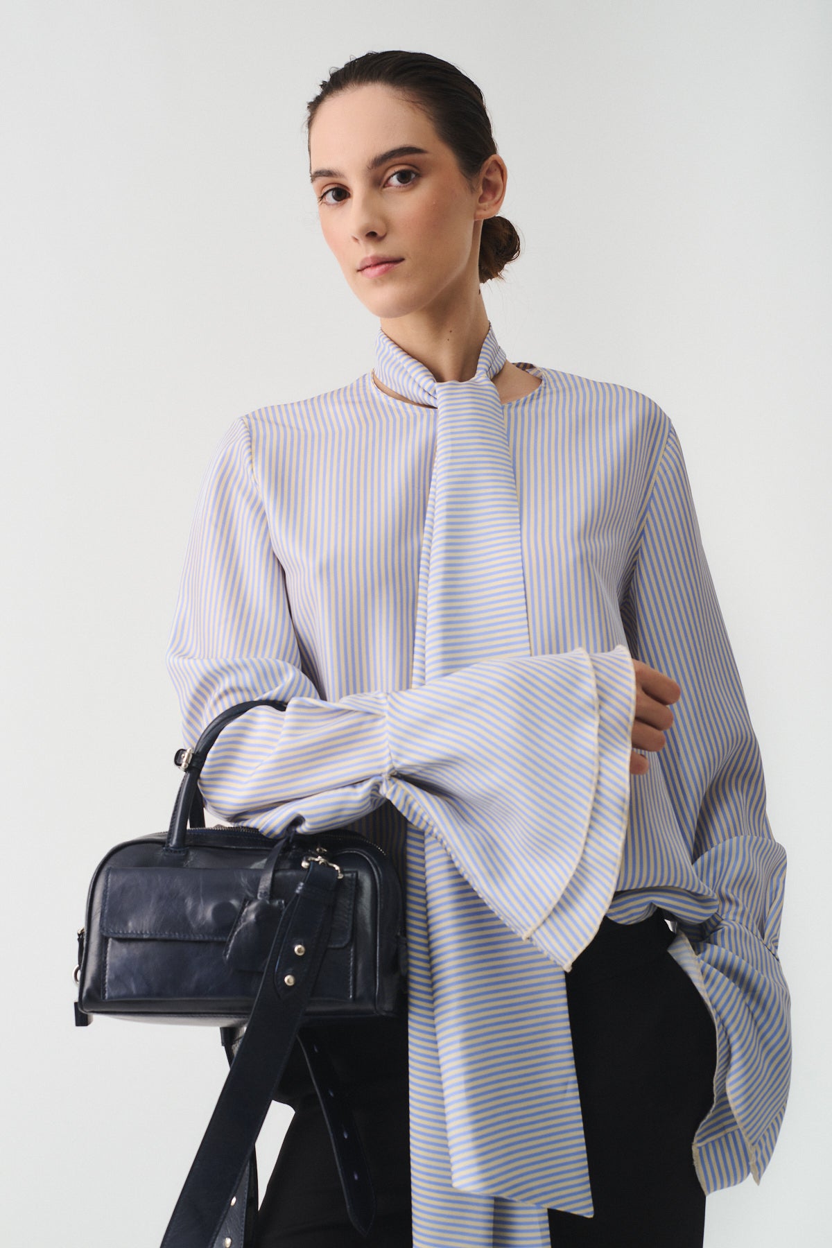 Model wearing a stylish striped blouse and holding a mini Vitello bag, showcasing elegant fashion.