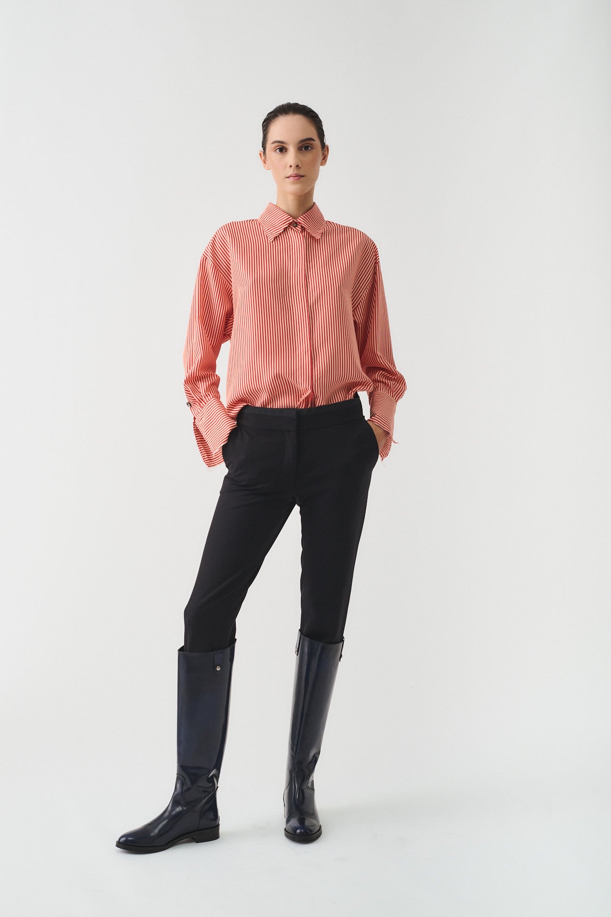 Modella che indossa la CAMICIA ISOTTA IN SETA CON BOTTONI GIOIELLO, pantaloni neri e stivali lucidi.