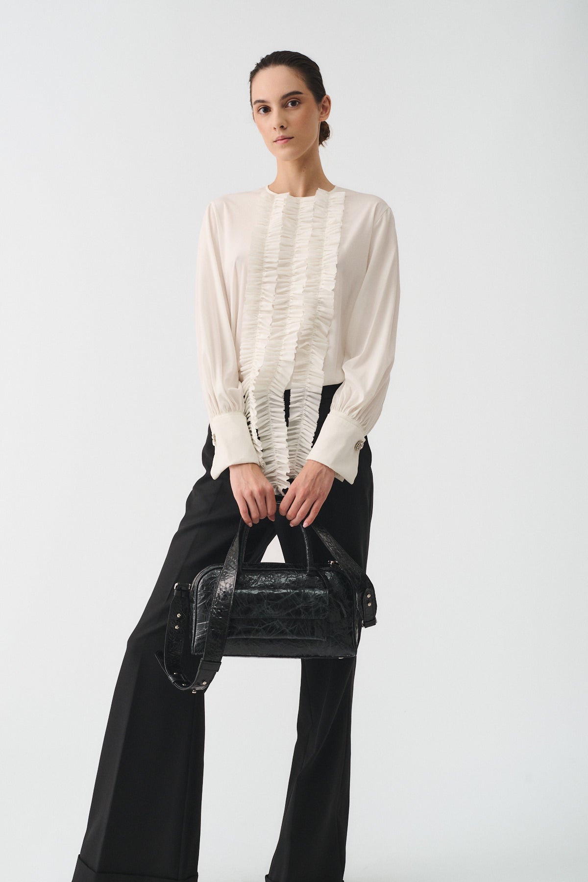 Model showcasing Zoe Small Vitello Strizzato bag, styled in elegant outfit with black trousers and cream blouse.
