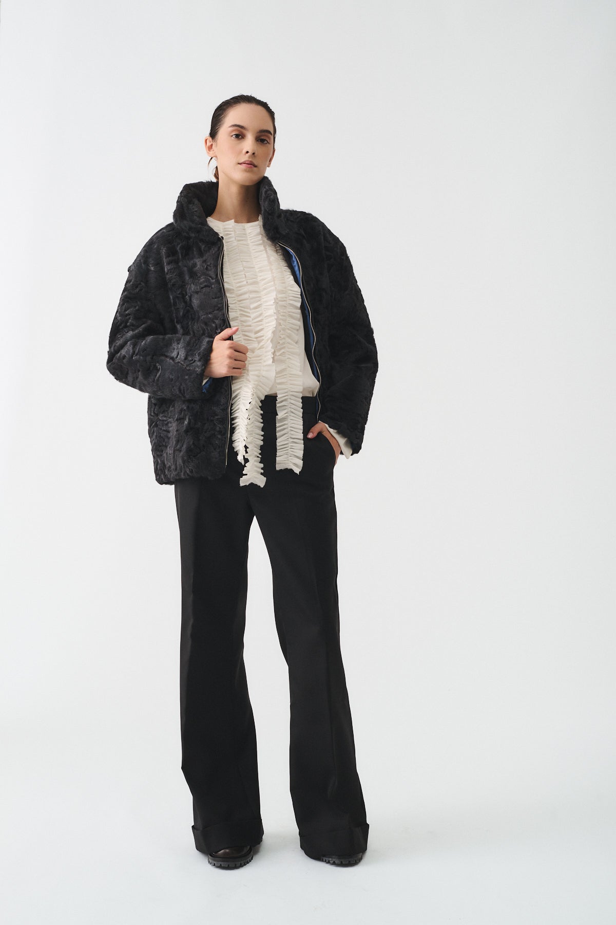 Model wearing BLOUSON ASTRAKAN UPCYCLE, a stylish black jacket with a textured finish, paired with a unique top and wide-leg trousers.
