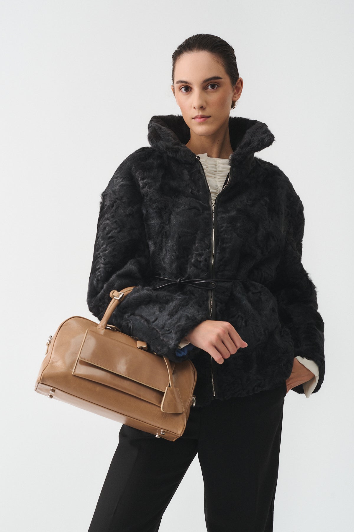 Model wearing a stylish black faux fur jacket and holding a tan handbag, showcasing modern fashion.