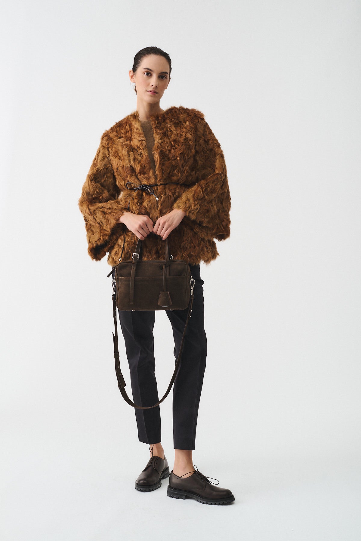 Model wearing a brown faux fur coat and holding a stylish handbag, showcasing modern fashion.