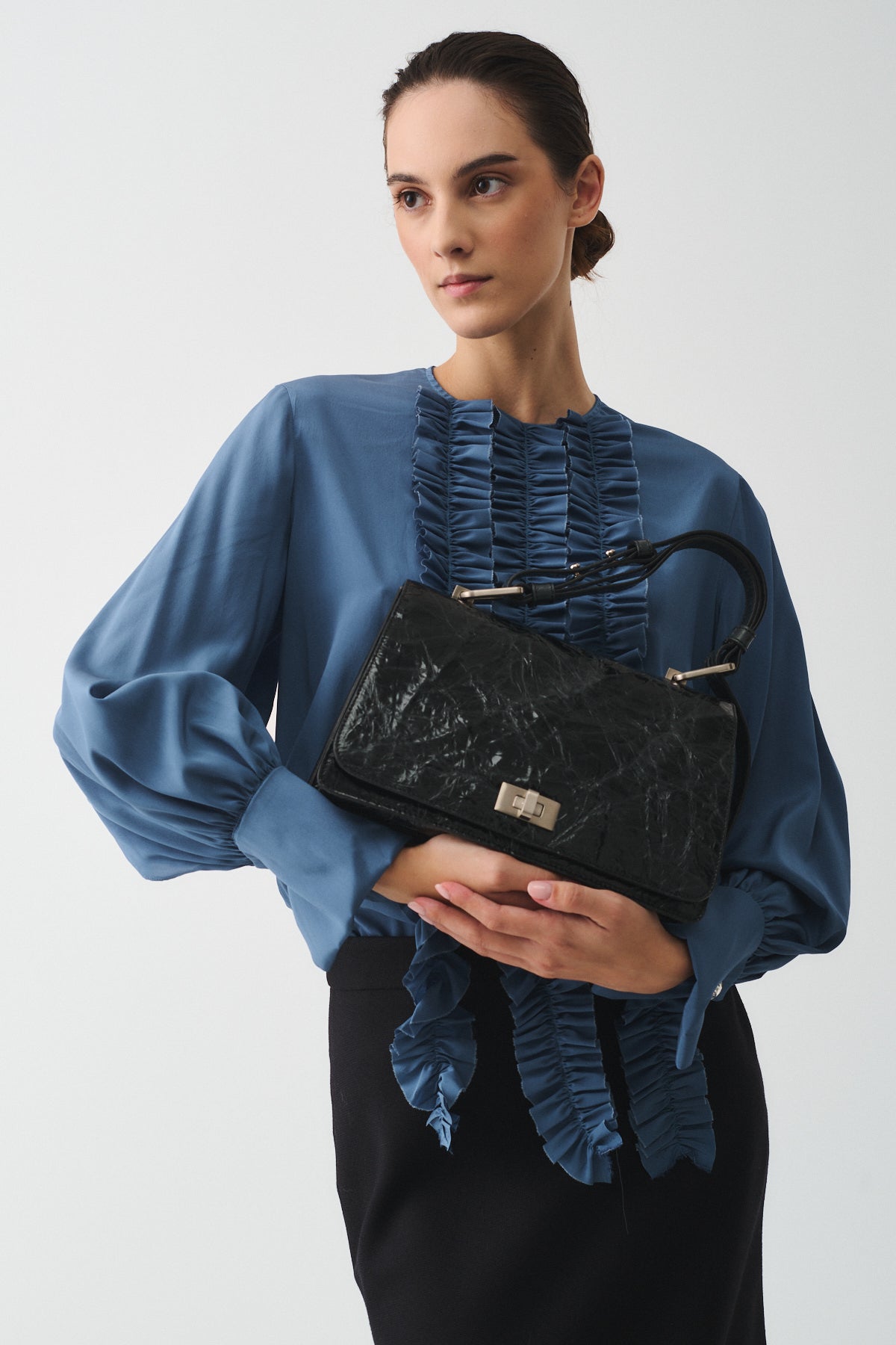 Model showcasing the Queen Vitello Strizzato handbag, wearing a stylish blue blouse and black skirt.