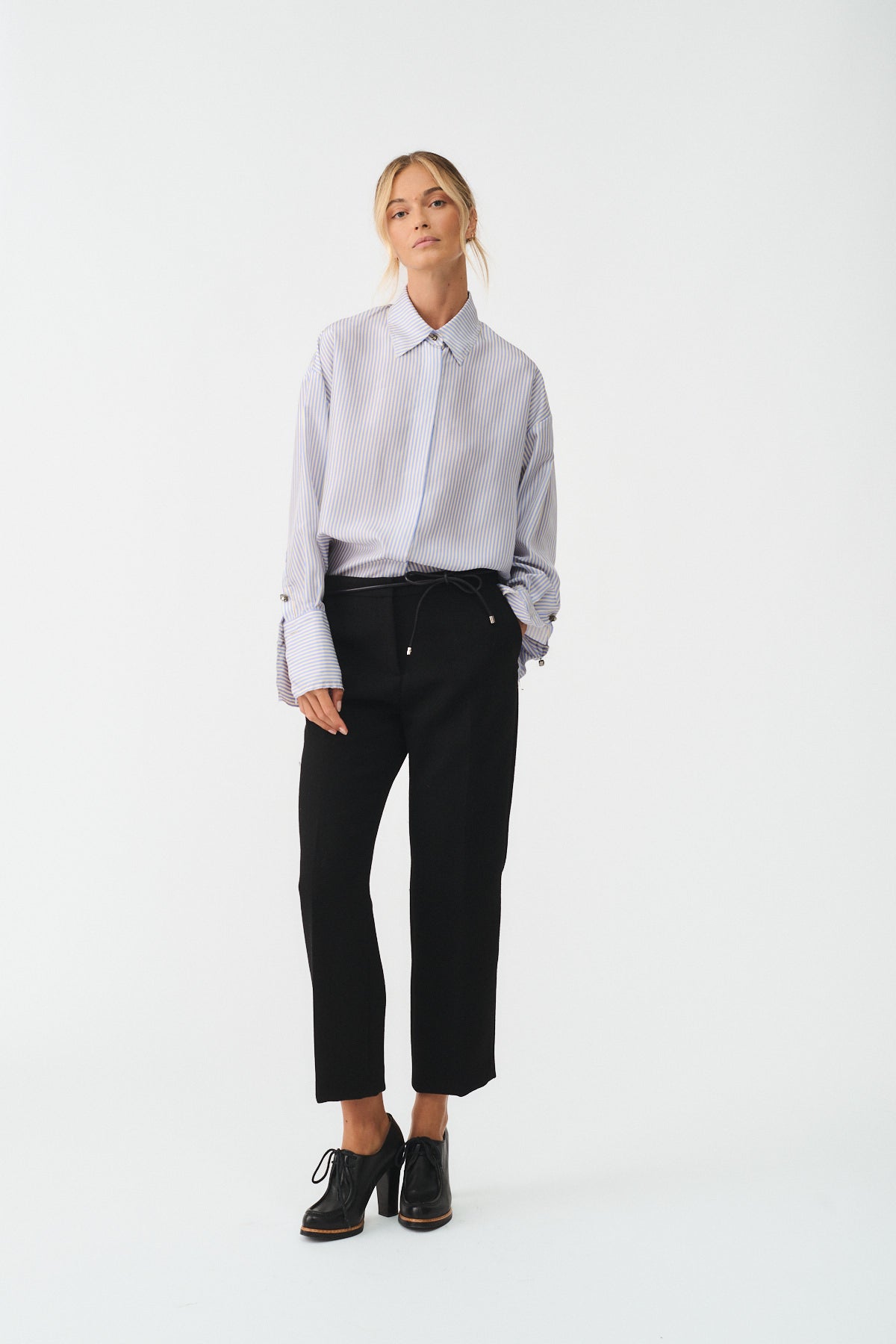 Giovane donna in camicia isotta in seta con bottoni gioiello, indossando pantaloni neri eleganti.