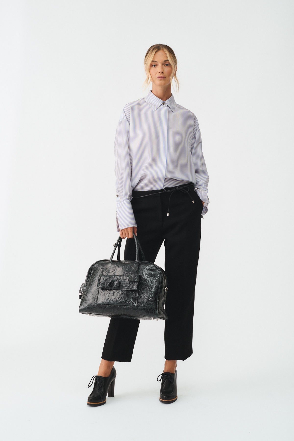 Modella in camicia oversized con borsa nera, presenta CAMICIA ISOTTA IN SETA CON BOTTONI GIOIELLO.