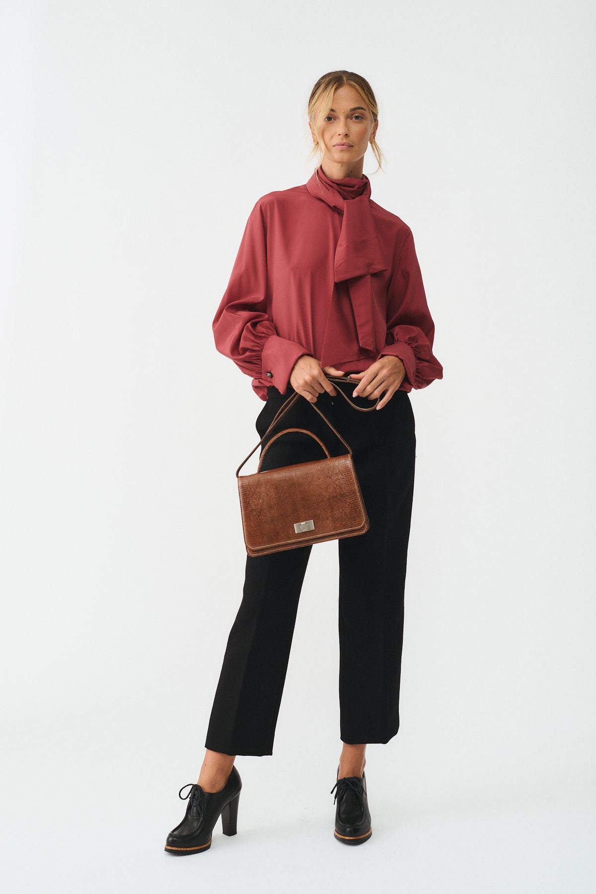 Woman in a stylish red blouse and black pants holding a Queen Tejus Recycle handbag.