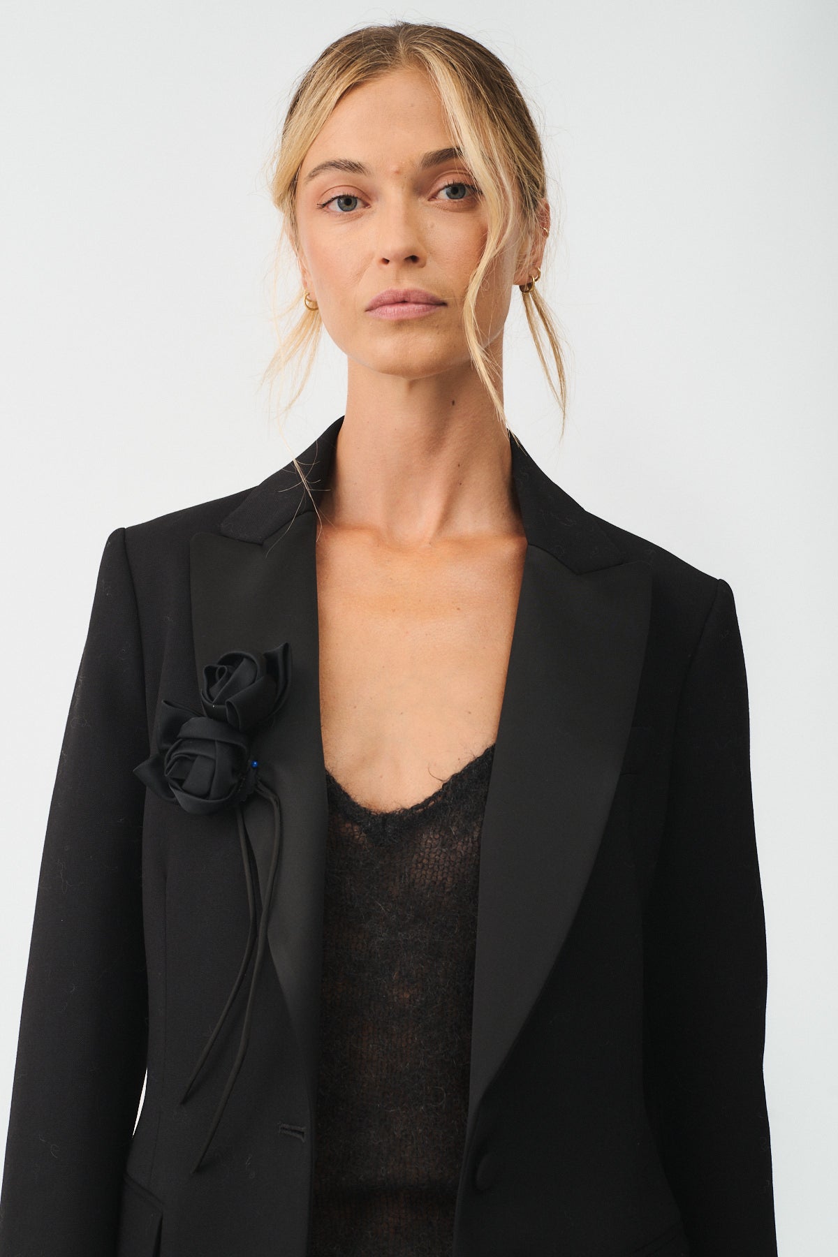 Elegant model showcasing a black blazer adorned with a rose fabric brooch, highlighting contemporary sophistication.