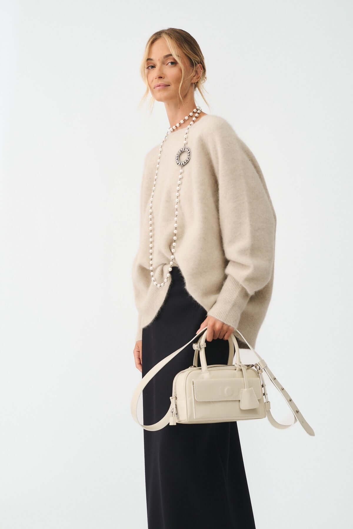 Modella che indossa la COLLANA MOD. 39 con perle e strass, abbinata a un maglione beige e una borsa elegante.