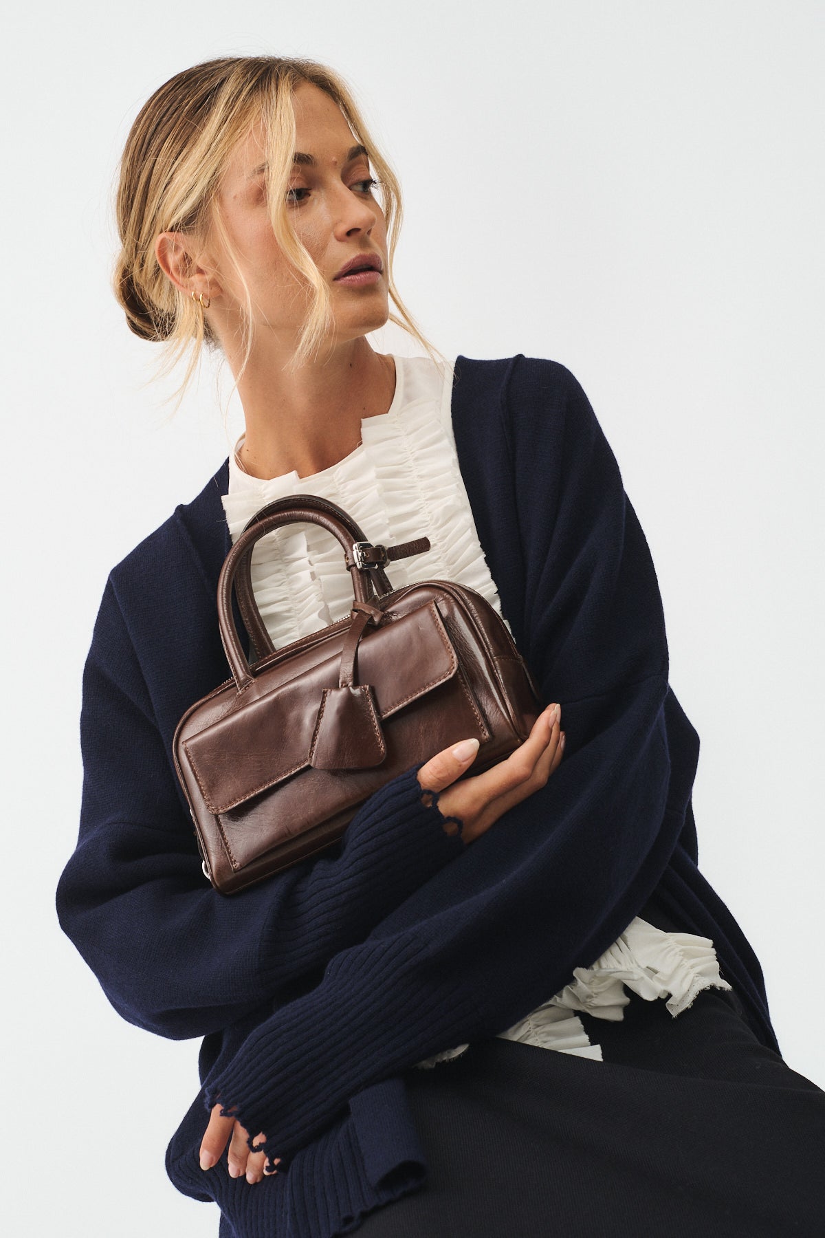 Woman in navy cardigan holding Zoe Mini Vitello Semilucido handbag, showcasing its elegant design and compact size.