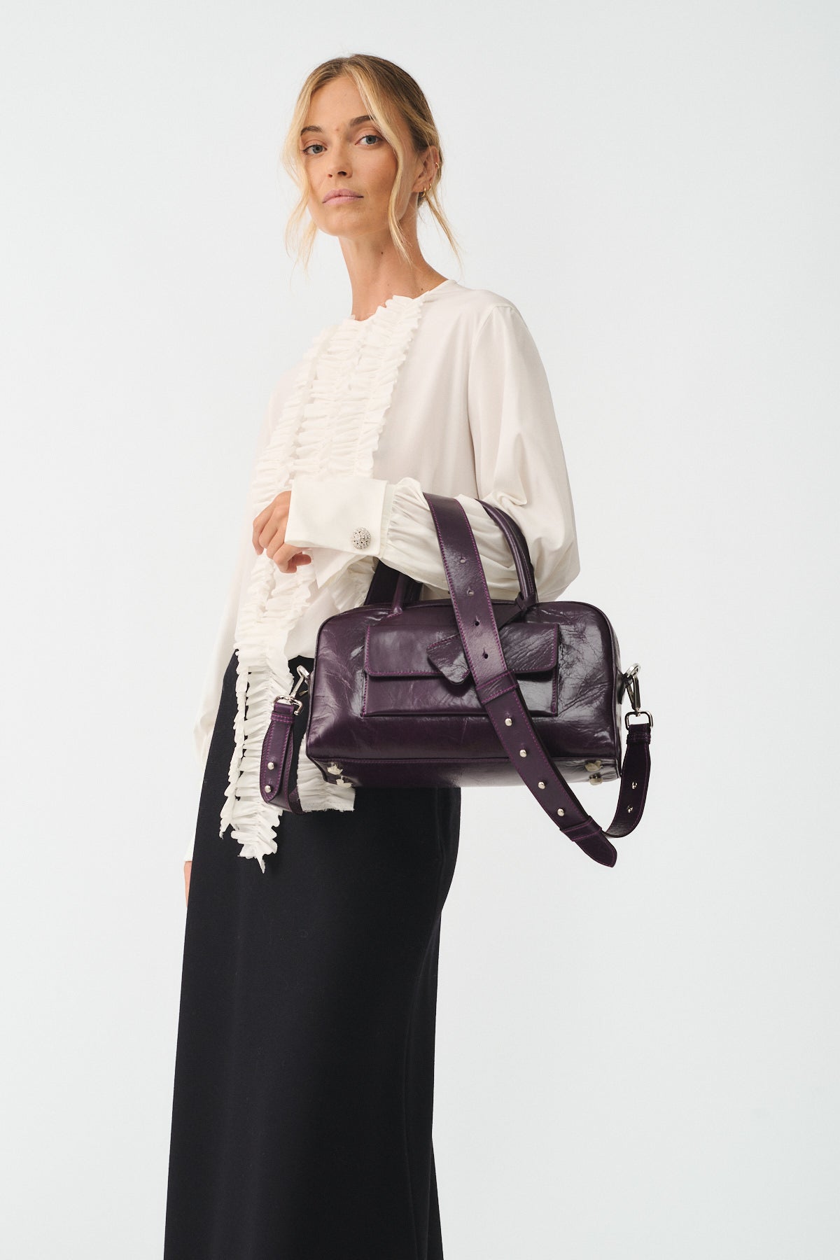 Model showcasing the small Zoe vitello semilucido bag in deep purple, styled with a chic white blouse and black skirt.