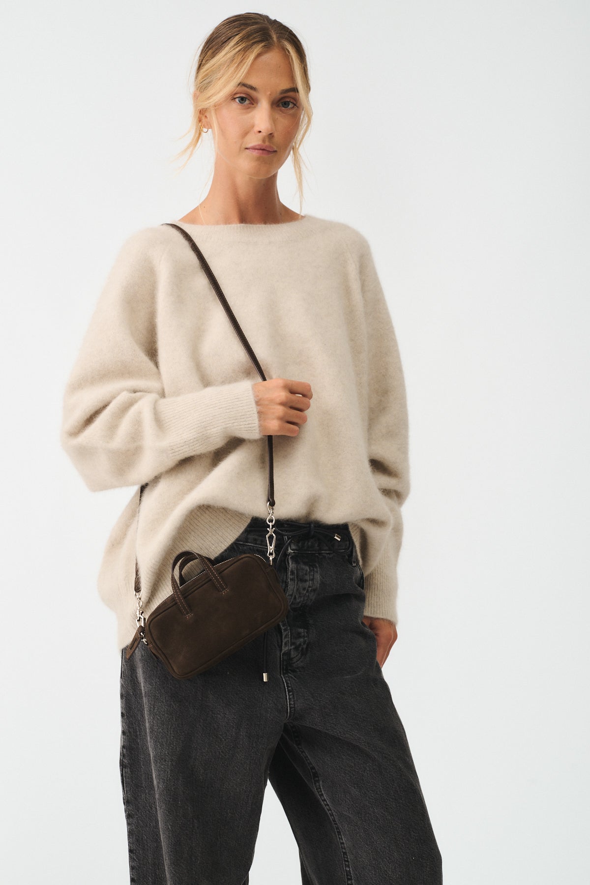 Woman in a cozy beige sweater and black jeans holding a small brown micro bag.