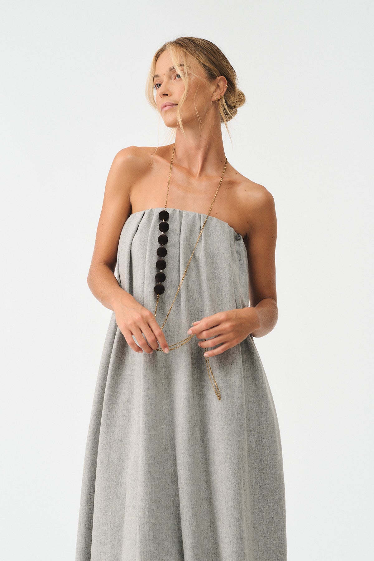 Woman wearing a modern gray strapless dress with a stylish necklace, showcasing a blend of elegance and contemporary fashion.