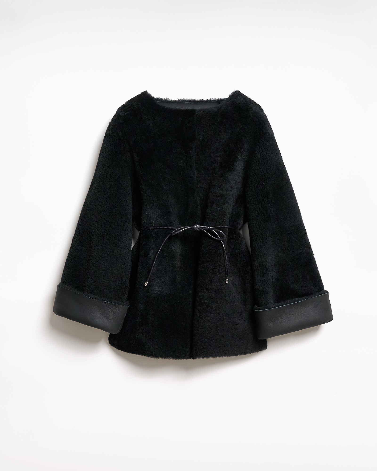 Reversible upcycled shearling coat in black with wide sleeves and a belt, showcasing a modern and elegant design.