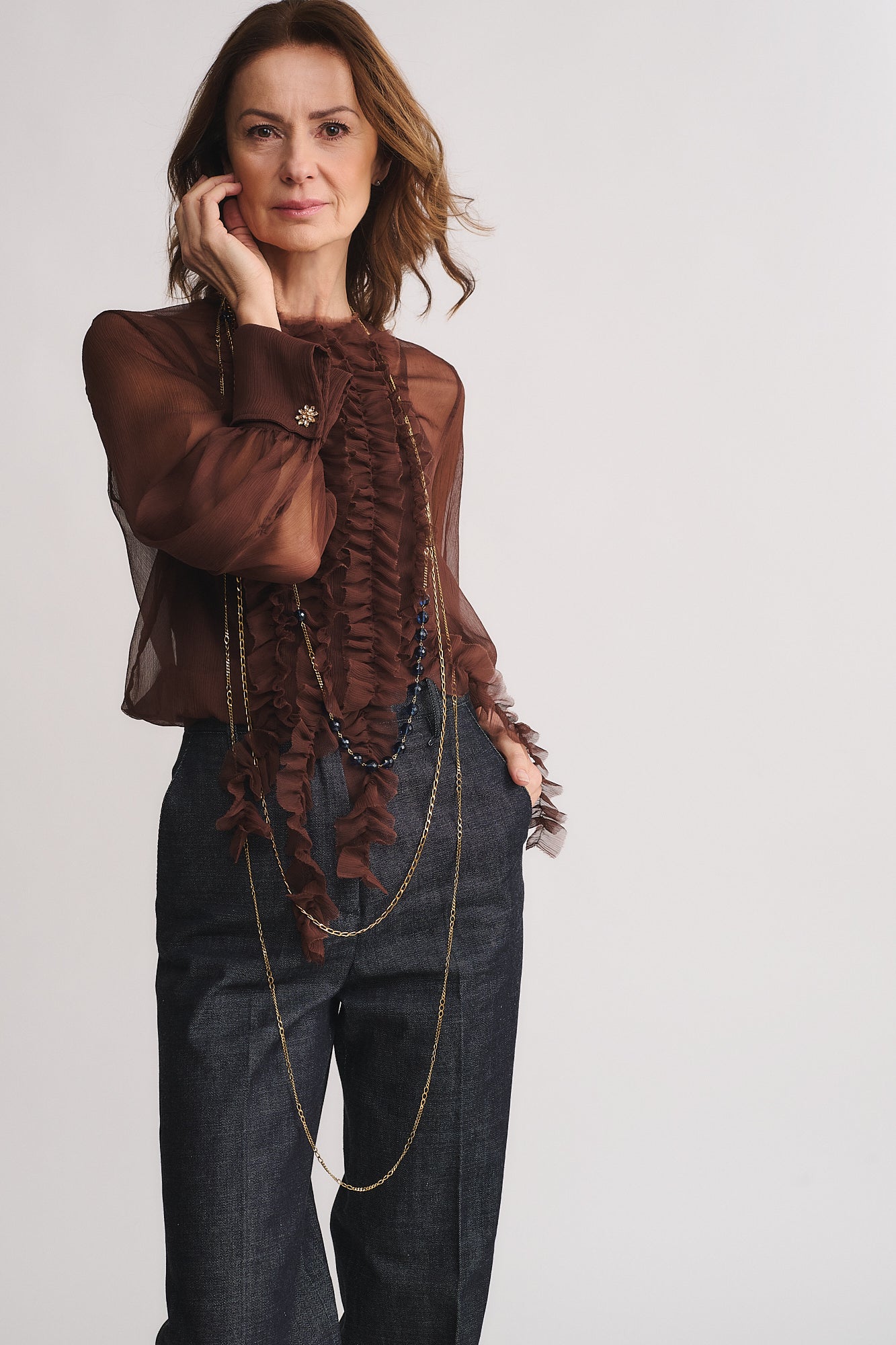 Moderna donna con collana COLLANA MOD. 31, camicia trasparente marrone e pantaloni eleganti, stile raffinato e contemporaneo.