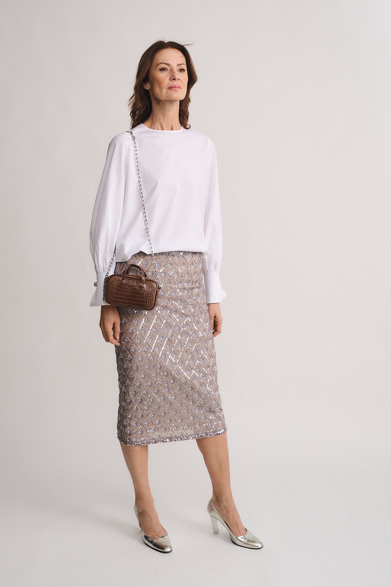 Woman wearing a white sweater and a silver sequined skirt, holding a MICRO BAG NINA MEDIUM COCCO RECYCLE.
