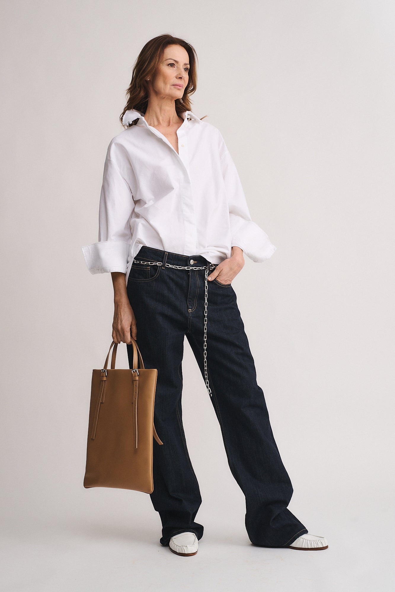 Woman holding AMELIE PORTACOMPUTER bag, dressed in a white shirt and dark jeans, exuding elegance and professionalism.