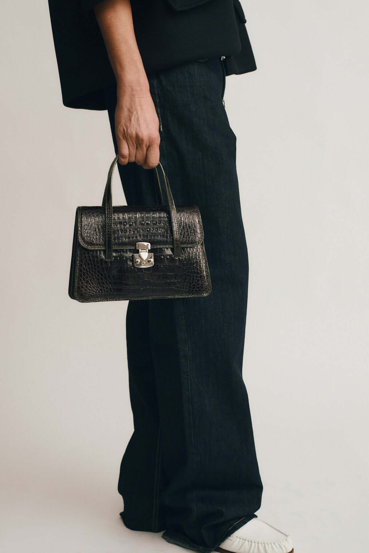 Model holding OFELIA COCCO RECYCLE EDITION black handbag with crocodile texture, styled with casual black jeans.