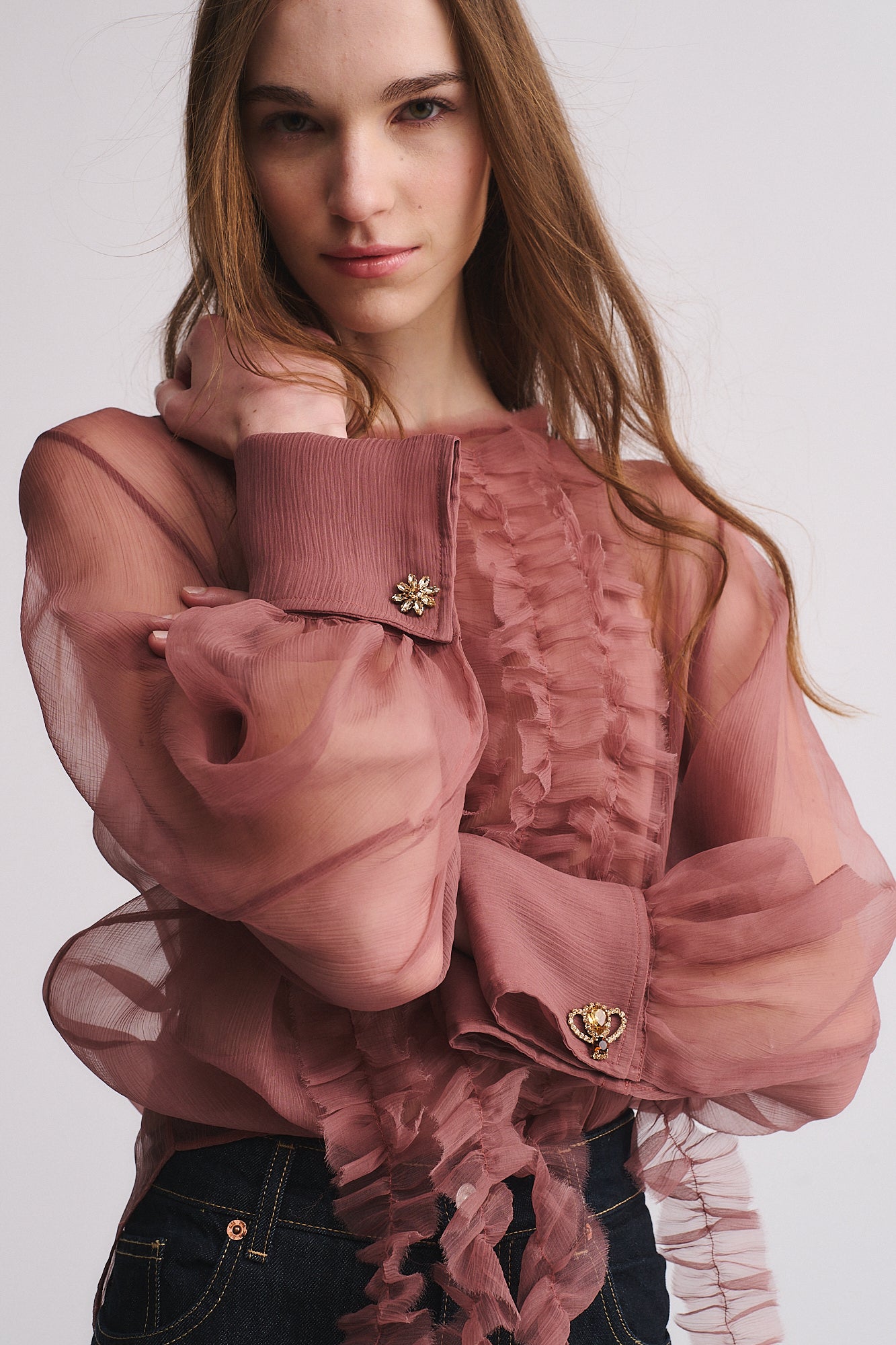 GEMELLI FIORE+APE REGINA displayed on a model wearing a pink sheer blouse with ruffled details.