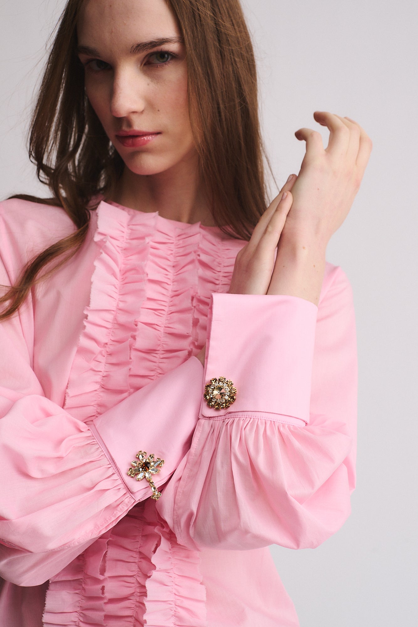Model wearing a pink blouse with ruffled details and embellished cuffs featuring GEMELLI FIORE-CROCE.