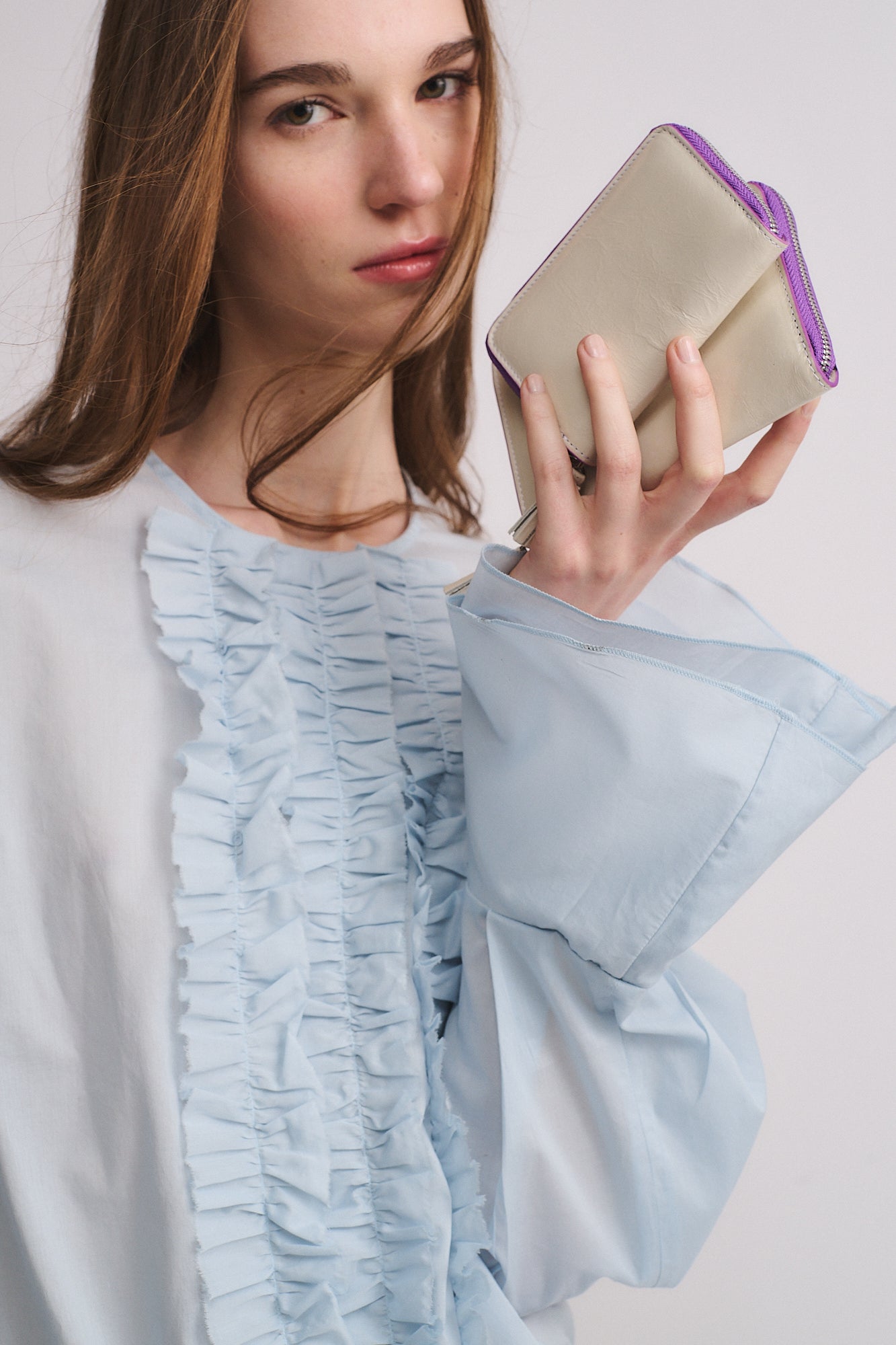 Modella che tiene il PORTAFOGLIO ZIP MINI in vitello con lamina e chiusura con zip viola.