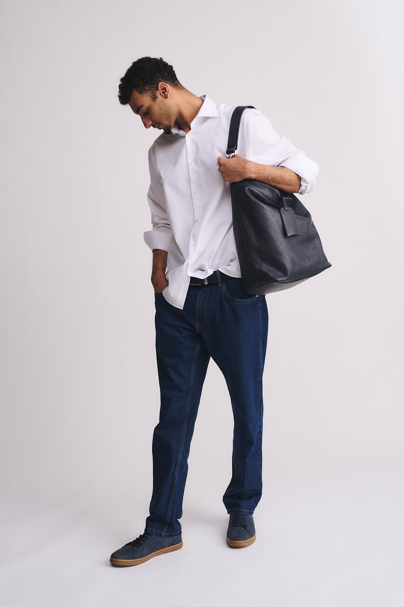 Uomo che indossa la borsa FORD in pelle, abbinata a una camicia bianca e jeans blu, per un look moderno.