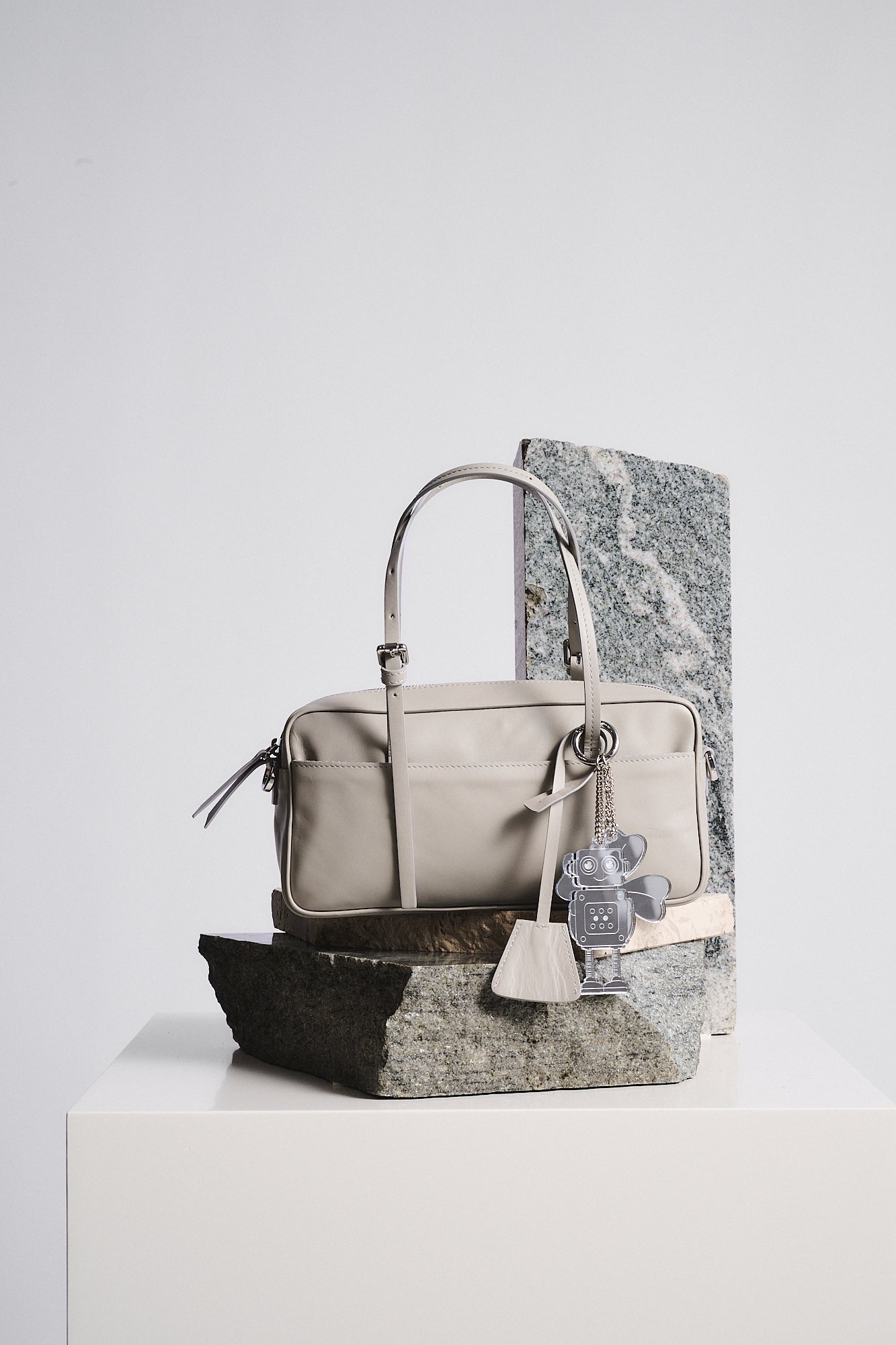 CHARMS PLEXI QUADRIFOGLIO attached to a fashionable beige handbag placed on textured rocks.
