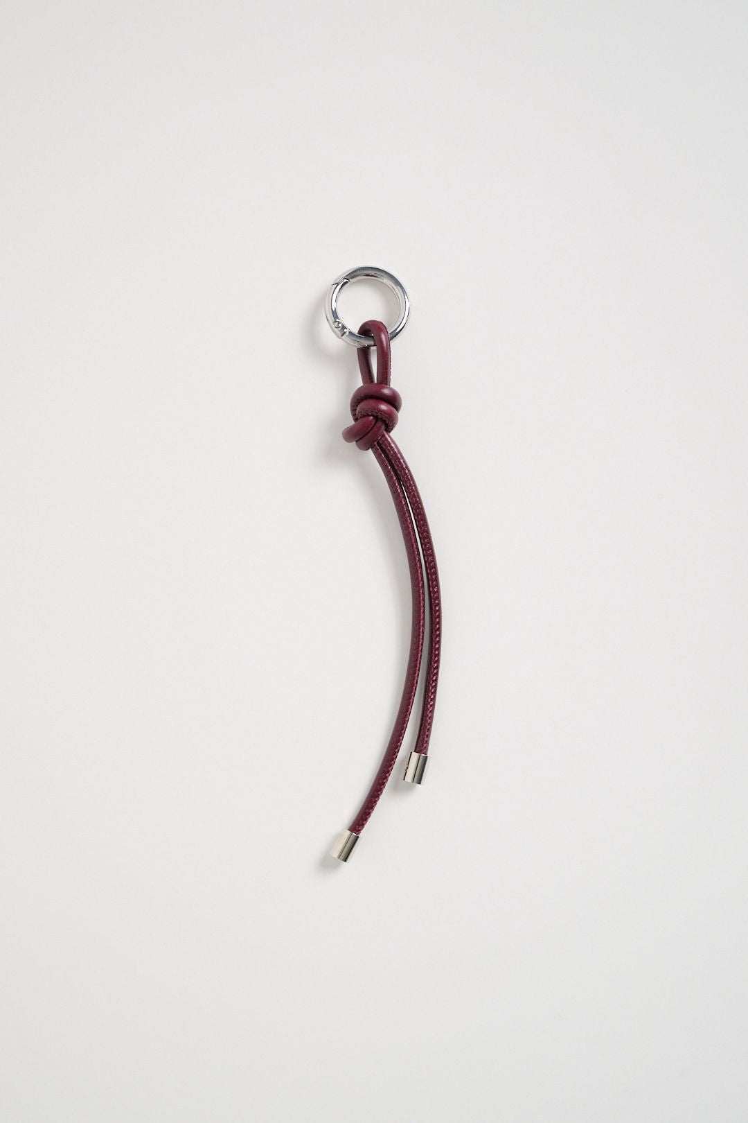 Charm a forma di nodo in pelle rossa con anello metallico e terminali in ottone.