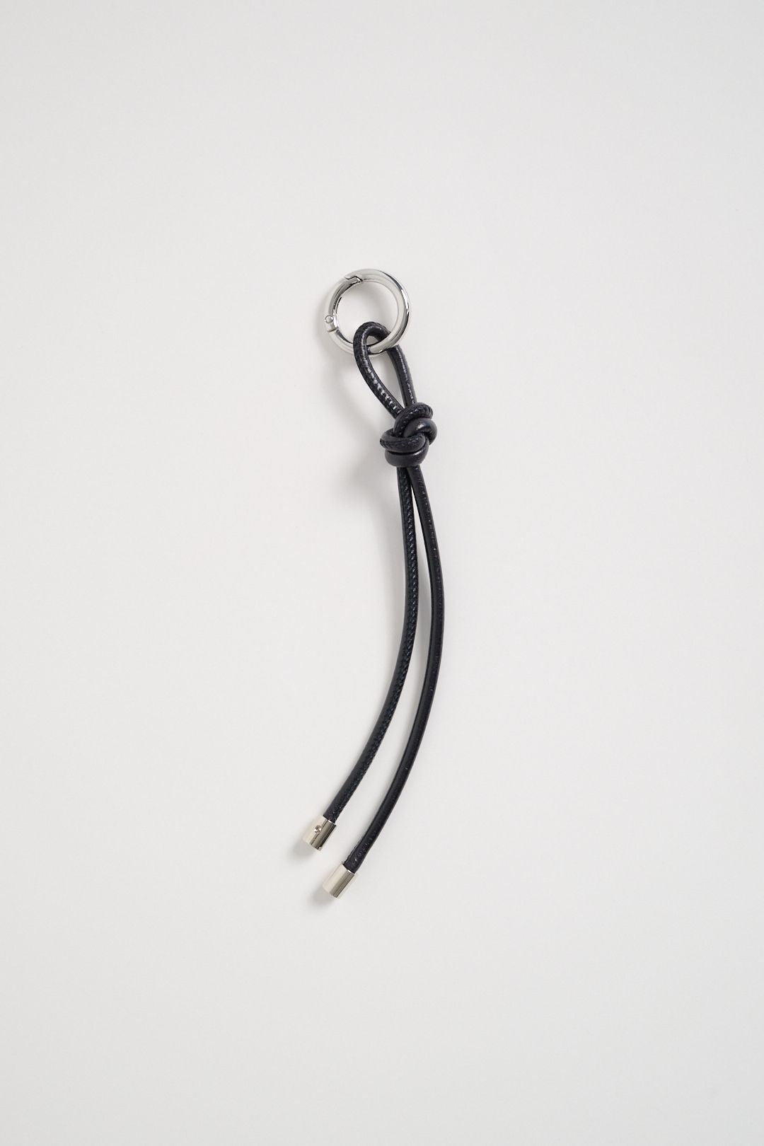 Charms tubolare in pelle nera con nodo e terminali in ottone color nickel, anello metallico apribile.