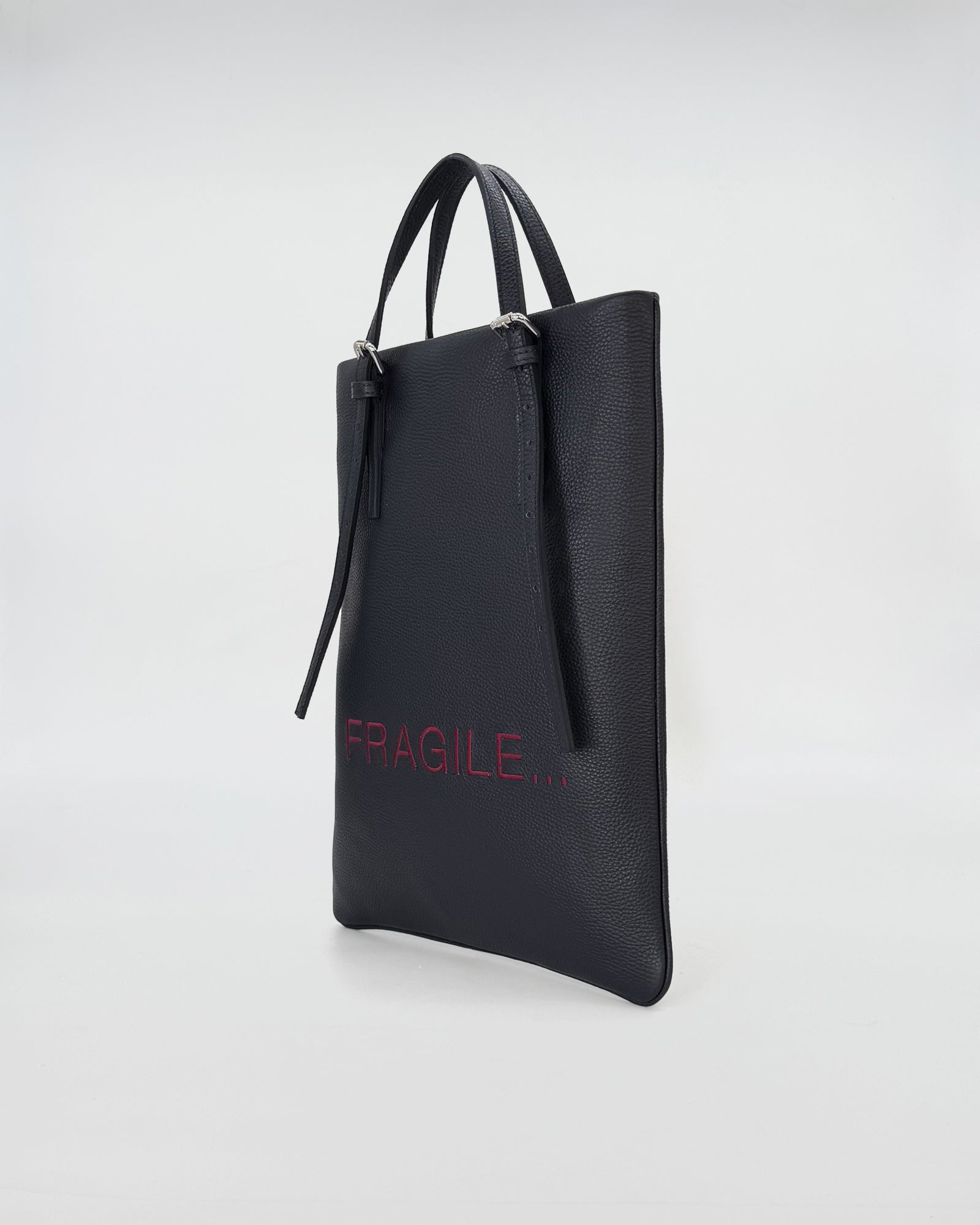Black leather handbag with 'FRAGILE...' embroidered in red, designed for work and versatile use.