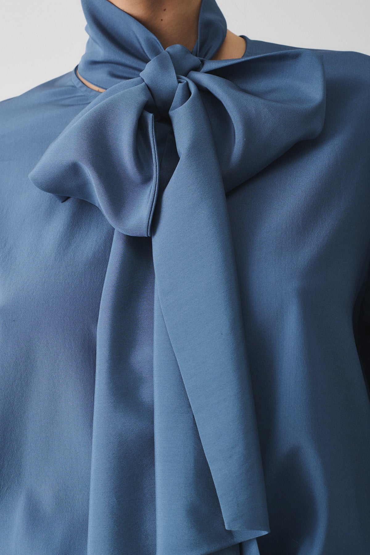 Dettaglio della camicia Charlotte in seta con sciarpa, elegante nodo in tessuto blu.