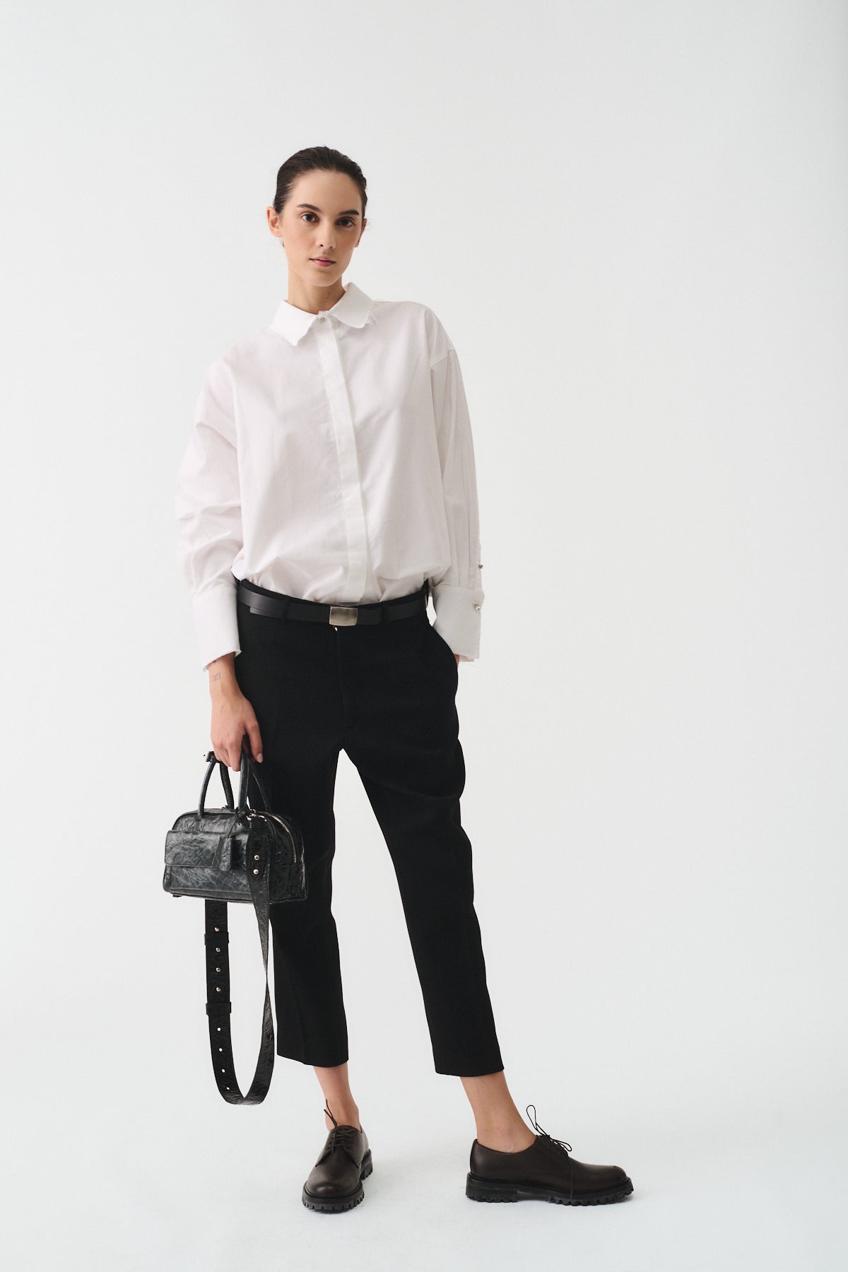Modella che indossa una camicia cotone oxford bianca con pantaloni neri e una borsa nera.
