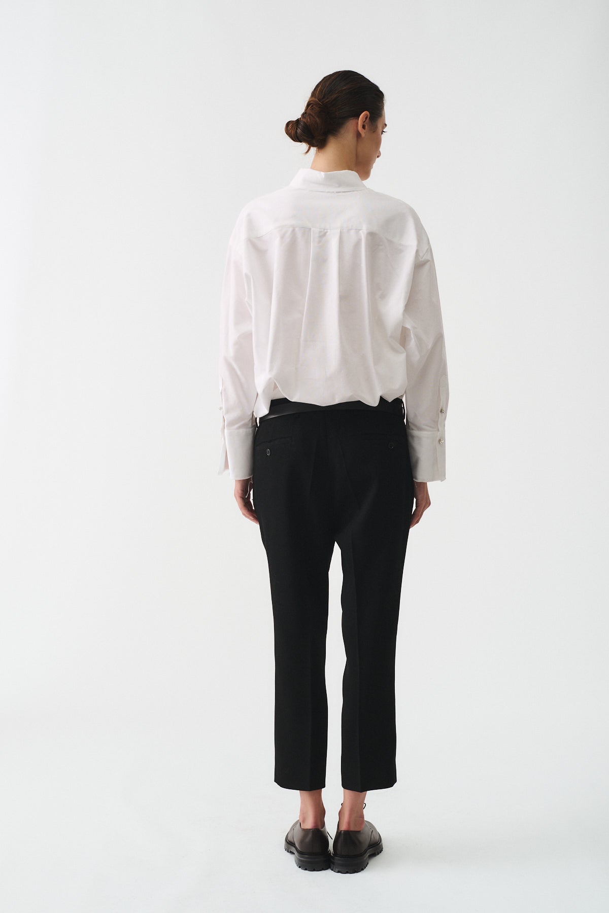 Uomo che indossa una camicia cotone oxford bianca oversize, vista da dietro, abbinata a pantaloni neri.