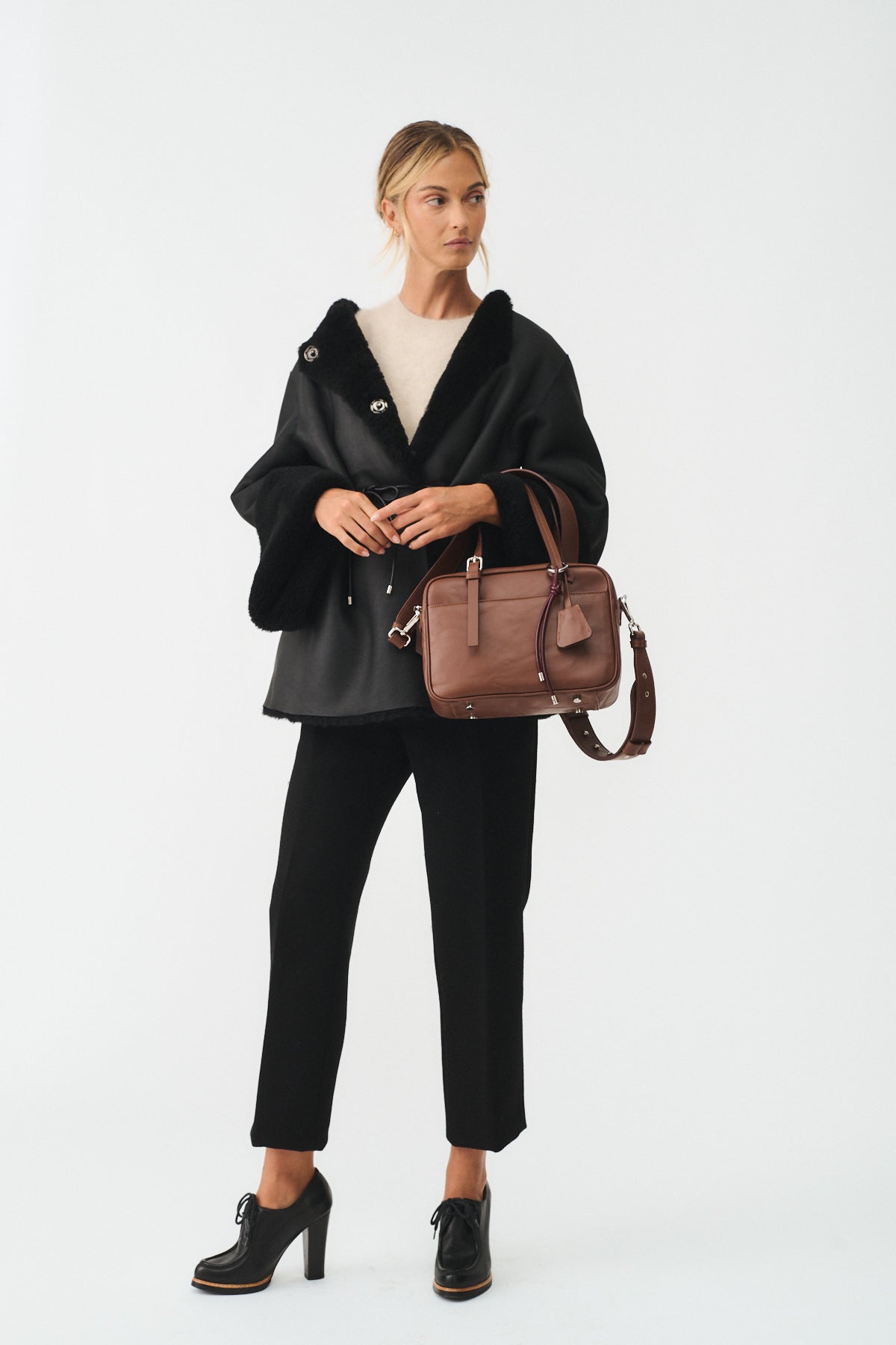 Model wearing a black coat and pants, holding FRIDA SMALL VITELLO LAVATO handbag for a stylish look.
