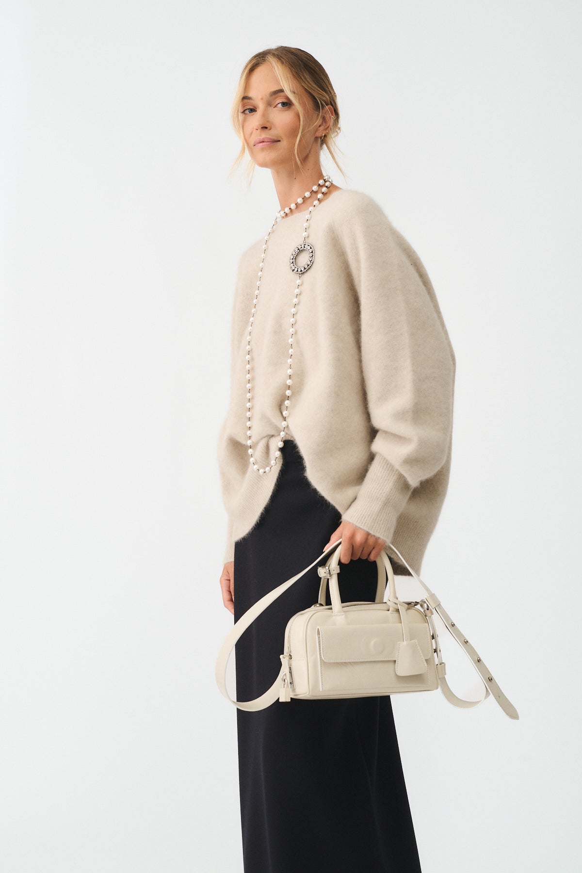 Woman wearing a beige sweater and black skirt, holding a mini Vitello bag for a stylish look.