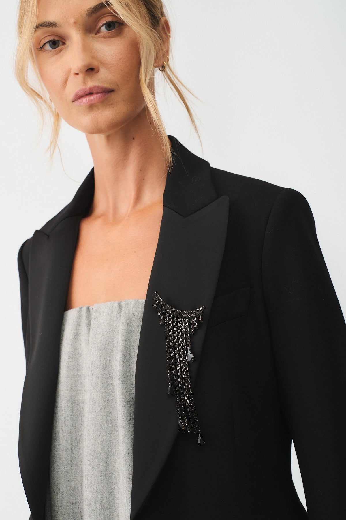 Close-up of woman wearing a black blazer adorned with a crystal fringe brooch, highlighting elegance and modern design.