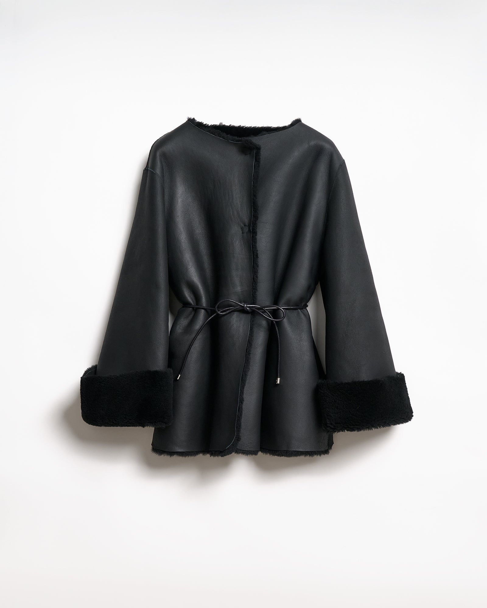 Reversible black shearling coat with V-neck and regular fit, featuring elegant tie belt and contrasting cuffs.
