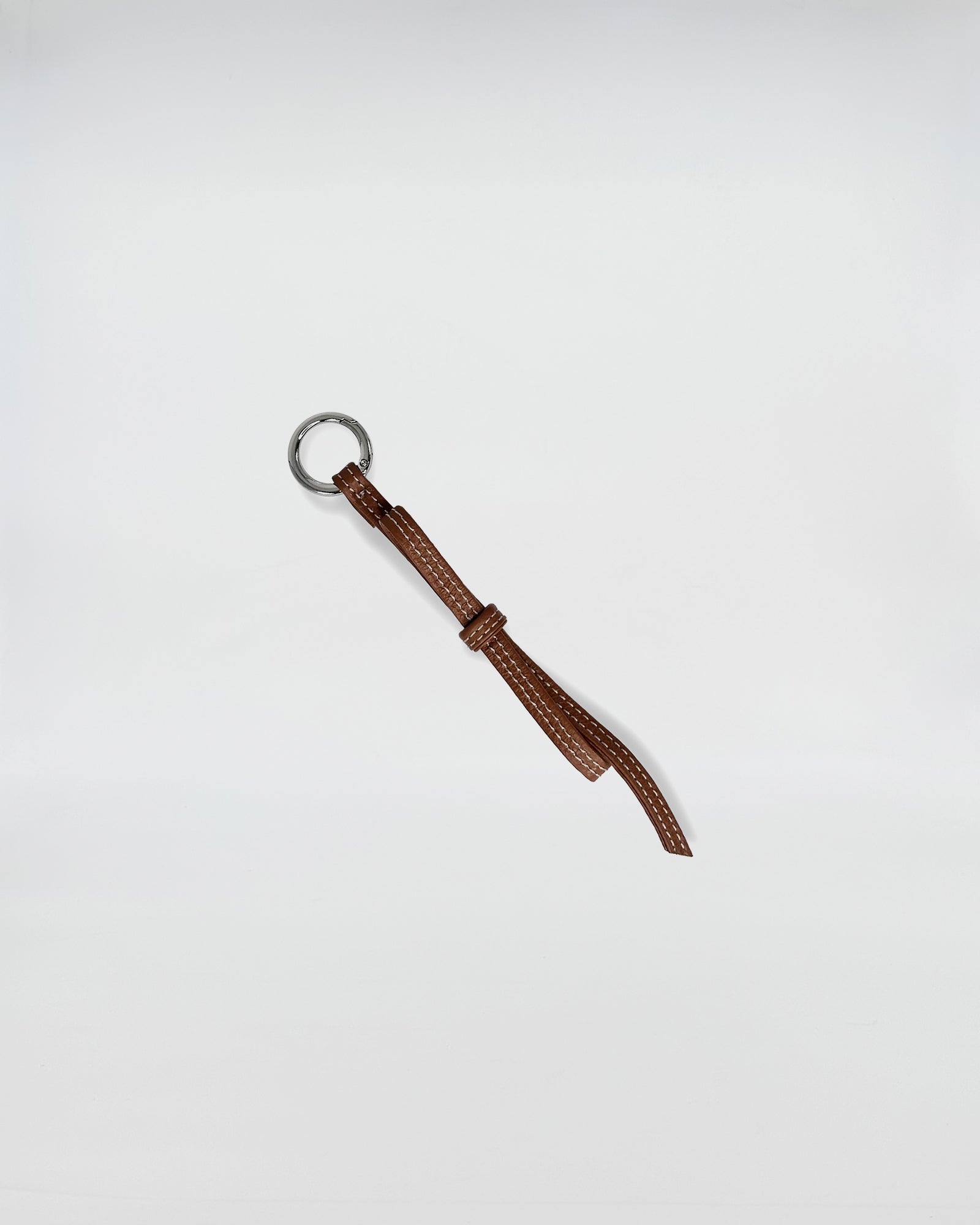 CHARMS IN PELLE FIOCCO in brown leather with a metallic ring, adding a playful touch to accessories.