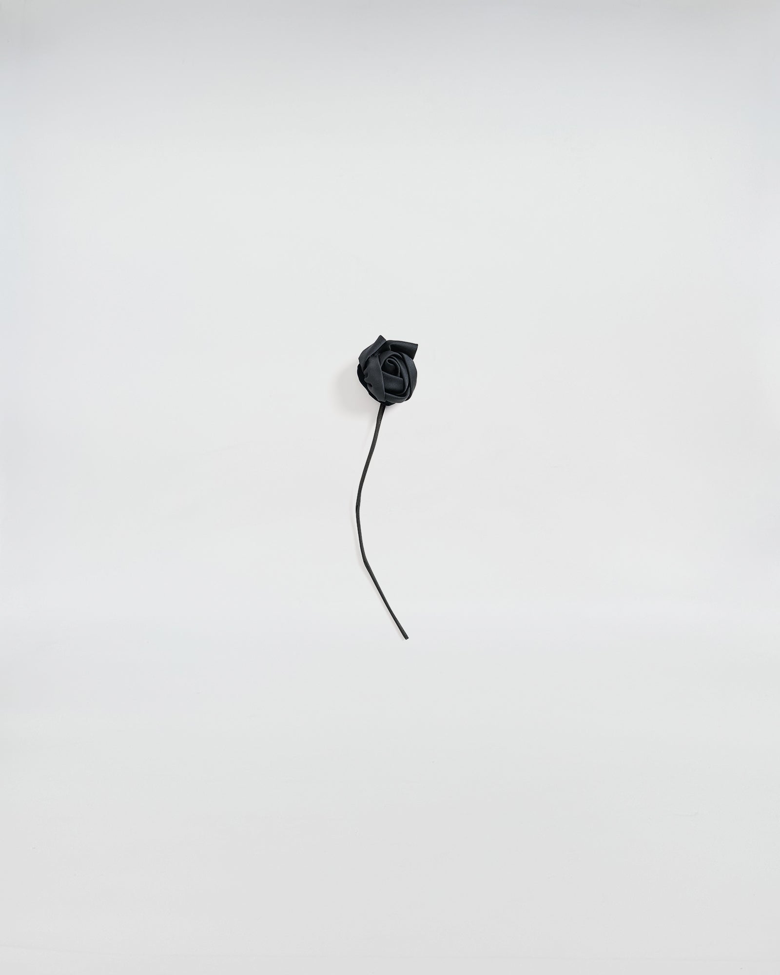 Elegant black satin rose brooch with a delicate stem on a light background.