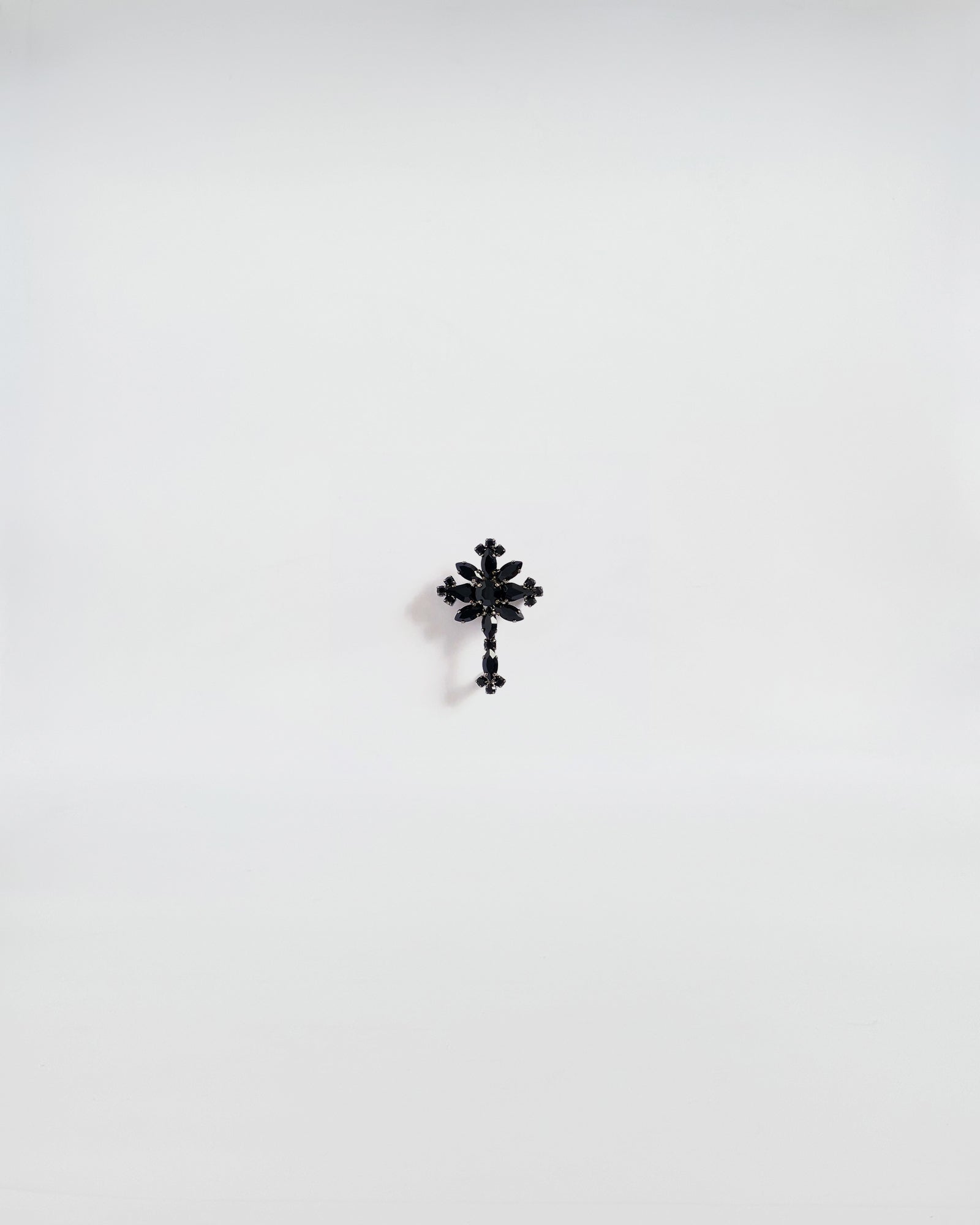 SPILLA IN STRASS CROCE, brooch with black stone and gunmetal finish on a white background.